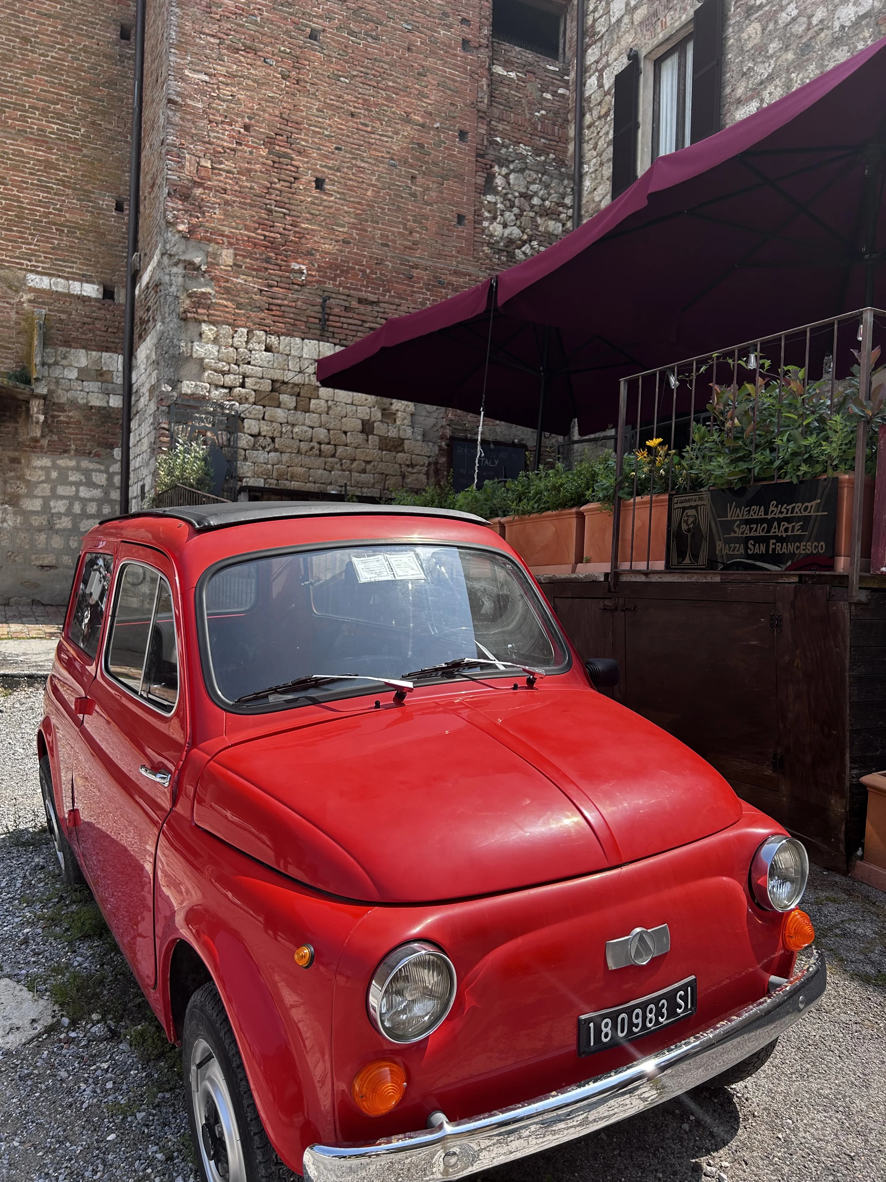 A red vintage Fiat 500 parked on a cobblestone street in Montepulciano